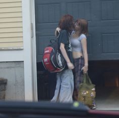 two young women standing in front of a garage door with their backpacks over their shoulders