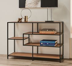 a shelf with books on top of it in front of a wall mounted painting and lamp