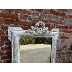 an ornate white framed mirror against a brick wall