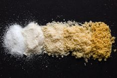 three different types of powdered food on a black surface with one yellow and the other white