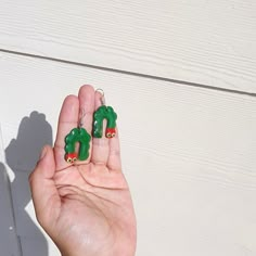 a person is holding two green earrings in their hand and the other one has a red heart on it