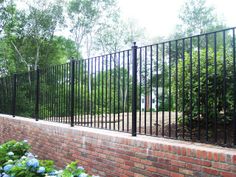 a brick wall and black iron fence in front of a house with blue hydrangeas