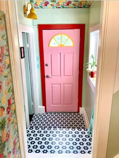 a bright pink door in the entryway to a colorful bathroom with black and white floor tiles