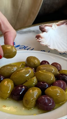 a woman is picking up some olives from a white plate with green and black olives on it