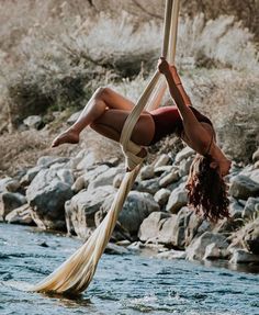 a woman is hanging upside down on a rope in the water while holding onto a pole