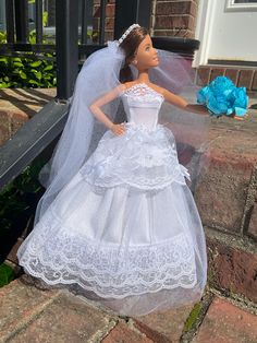 a barbie doll dressed in a white wedding dress and veil with blue flowers on the steps