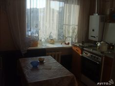 a kitchen with a table, stove and window in the corner that has curtains on it