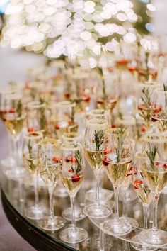 many wine glasses are lined up on a table with christmas decorations and greenery in them