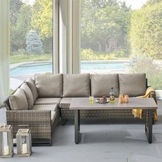 a couch and coffee table on a patio with large windows overlooking the pool in the background