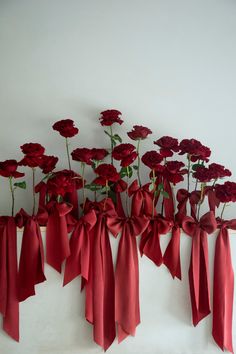 red flowers are arranged on a white wall with ribbons tied around them and hanging from the side