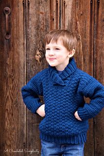 a young boy standing in front of a wooden door wearing a blue sweater and jeans