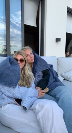 two women sitting on a couch wrapped in blankets