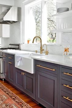 a kitchen with black cabinets and white counter tops, gold pulls on the faucets