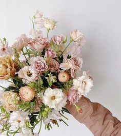 a hand holding a bouquet of pink and white flowers in it's left arm