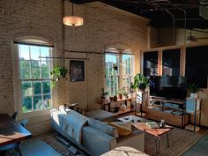 a living room filled with furniture and lots of windows next to a brick wall covered in plants