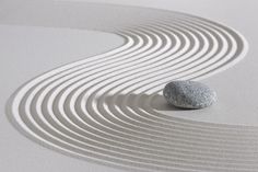 a rock sitting on top of a white sand covered ground with wavy lines in it