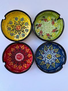 four colorful bowls with designs on them sitting next to each other in the middle of a white surface