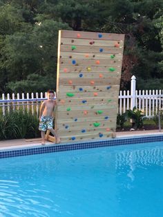 a young boy climbing up the side of a wooden wall next to a swimming pool