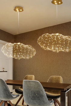 a dining room table with chairs and lights hanging from the ceiling above it, in front of a brown wall