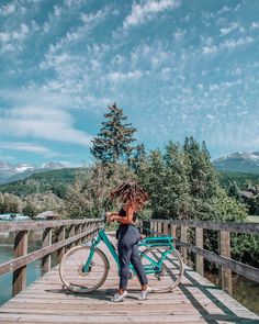 a woman with an umbrella standing on a pier next to a bike