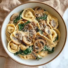 pasta with spinach and mushrooms in a white bowl on a beige cloth next to a spoon