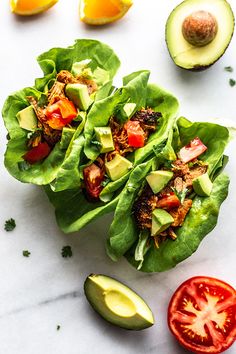 three lettuce wraps with avocado, tomatoes and other toppings on a marble surface