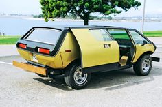 a small yellow car parked in a parking lot next to a tree and the ocean