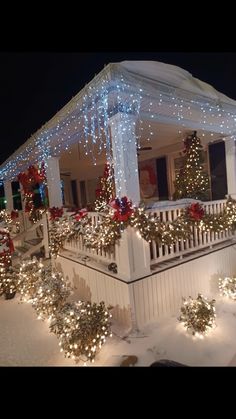 a house covered in christmas lights and decorated with garlands on the front porch at night