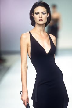 a woman in a black dress walking down a runway