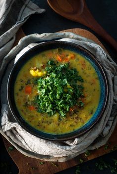 a bowl of soup with vegetables and herbs in it on a wooden table next to a spoon