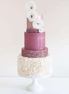 a three tiered cake with pink and white flowers on the top, sitting on a pedestal