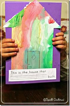 a child holding up a house made out of construction paper with words written on it