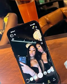 a cell phone with an image of two women on the screen next to a drink