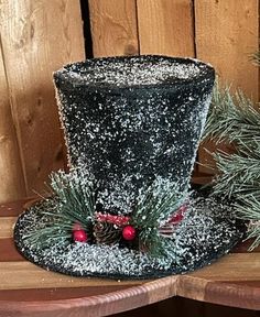 a black top hat decorated with pine cones and red berries sits on a wooden table