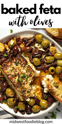 baked feta with olives in a white bowl on a striped tablecloth next to bread