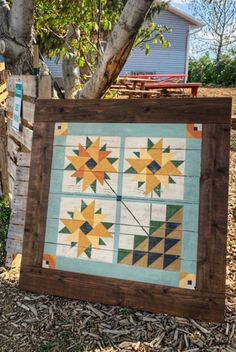 a wooden frame with a quilt hanging on it's side next to a tree