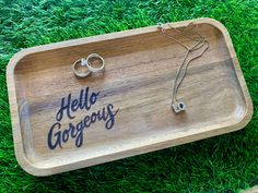 a wooden tray with two wedding rings on it and the words hello gorgeous written in cursive writing