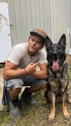 a man kneeling down next to a german shepard dog in front of a metal building