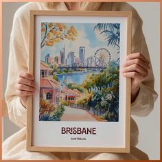 a woman holding up a framed poster with an image of a city in the background