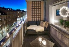 a balcony with a couch, table and lights on the windowsill at night time