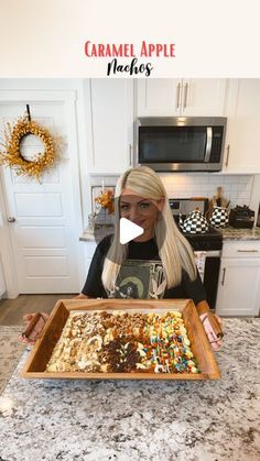 a woman holding a tray full of food in front of a kitchen counter with the words caramel apple macaroni and cheese on it