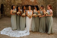 a group of women standing next to each other in front of a brick wall holding bouquets