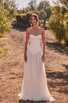 a woman in a white dress standing on a dirt road