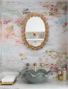 a bathroom sink under a round mirror next to a white counter top with gold faucet