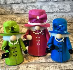 three colorful dolls are standing next to each other on a stone wall and one is wearing a pink hat