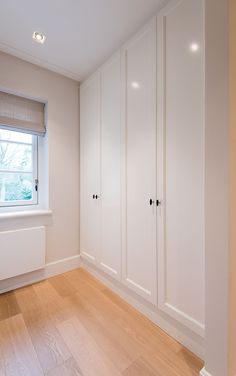 an empty room with white cupboards and wood flooring in front of a window