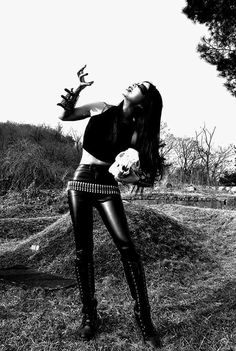 a woman in leather pants and boots is holding her hands out to the sky while standing on grass