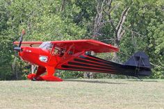 a small red and black plane sitting on top of a grass covered field next to trees