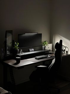 a computer desk with a monitor, keyboard and plant on it in a dark room