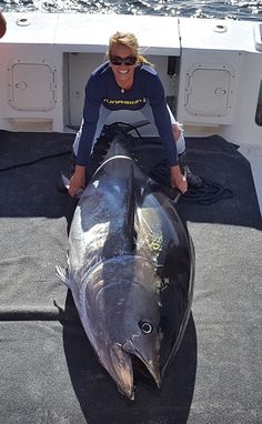 a woman kneeling down next to a large fish on a boat in the water,